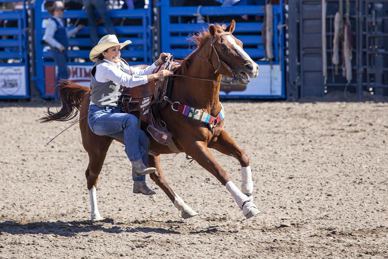 rodeo cowgirl dismounts from her running horse to rope a goat